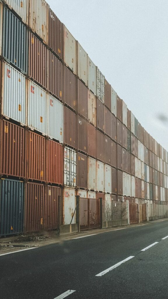 High-rise stack of shipping containers along an industrial road in foggy weather.